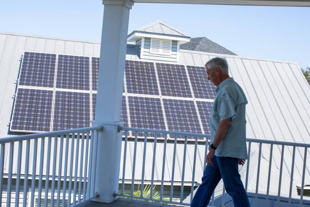 Jim Muhl walks to the edge of his porch with his solar power system behind him. 